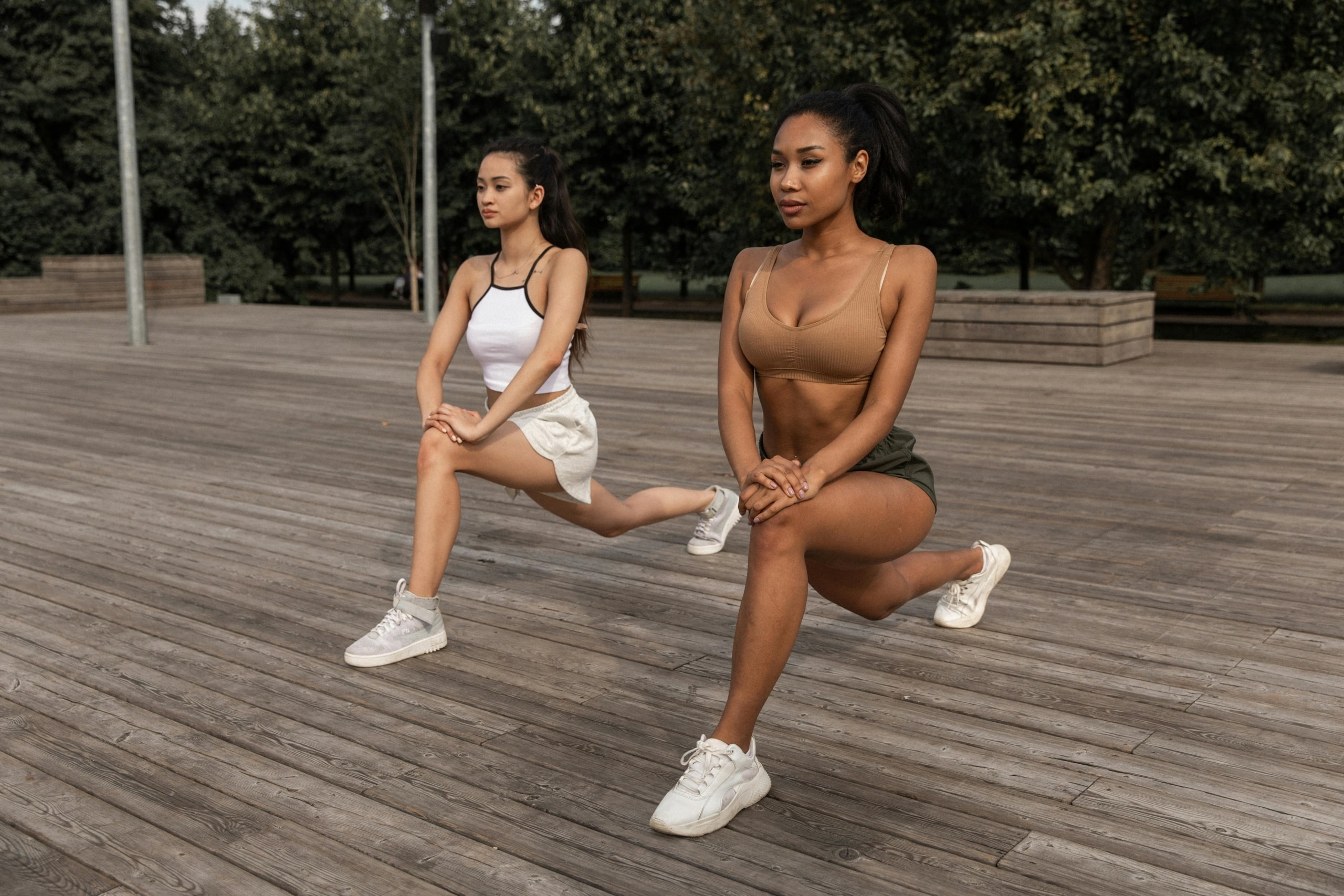 Two women performing lunges outdoors, demonstrating knee-strengthening exercises